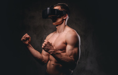 Fototapeta na wymiar Young sportsman with muscular body wearing VR headset training punches in virtual reality fight on dark background.