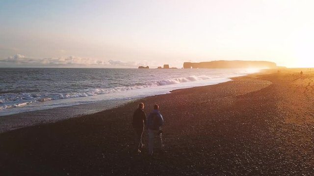 couple of tourists in Iceland walking on black sand beach at sunset