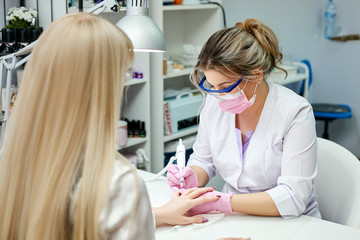 Fototapeta premium The nail master in lab coat does hardware manicure in the beauty salon. Removal of the gel varnish with a milling cutter.
