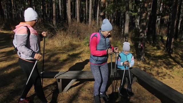 Woman do Nordic walking in nature. Girls and children use trekking sticks and nordic poles, backpacks. Family travels and goes in for sports. Kid is learning from mother and grandmother the proper
