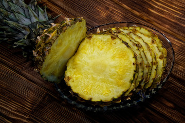 Slices of ripe pineapple in a transparent plate on a diagonal wooden background