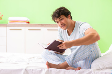 Fototapeta premium Young handsome student reading book in the bed 