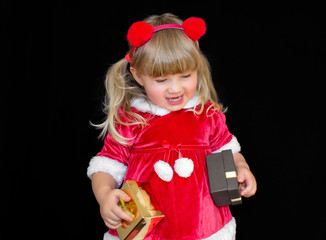 Little beautiful girl in a Christmas Santa suit, with fur balls on her head, holds gifts in her hands and rejoices. The concept of celebrating Christmas, New Year and gifts.