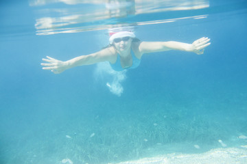 Fototapeta na wymiar Woman in Santa hat swimming underwater