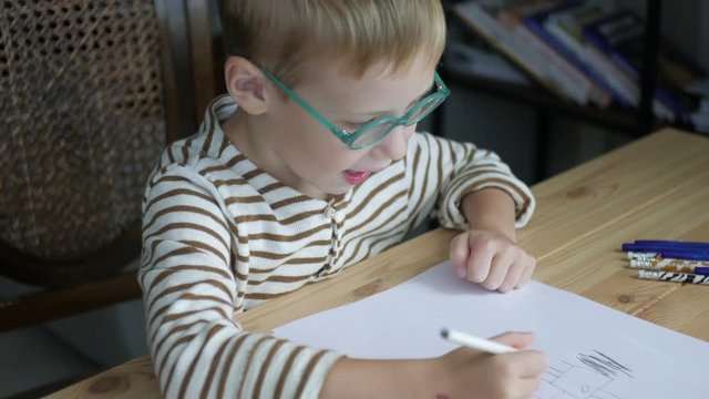 little boy with glasses draws sitting at the table