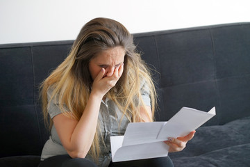 Woman reads negative news in a letter at home on the couch. The shaken business manager of received...
