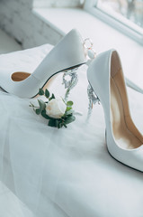 A pair of white wedding shoes with rings on a stool.