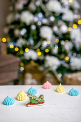 Gingerbread sleigh and meringue on the table in front of defocused lights of Christmas decorated fir tree. Holiday sweets. New Year and Christmas theme. Festive mood. Christmas Card