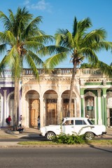 White car in front of Colonial style houses with palm trees in cuban city