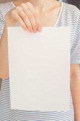 Caucasian woman in striped t-shirt hold a white blank paper sheet in hand