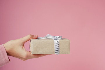 Woman hand holds gift box on a pink background