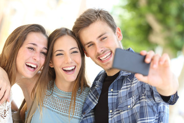 Three happy friends taking selfie together in the street