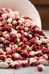 Seeds of two-color beans, scattered from a tilted white bowl, close-up, vertical.