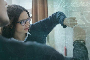 Two young college male and female students writting on the chalkboard during a math class.