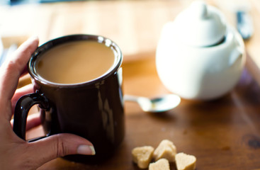 Having a cup of coffee closeup of womans hand holding a warm cup of coffee on wood table with sugar cubes and sugar pot in background