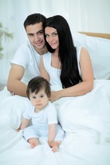Fototapeta premium Cute little boy with parents on the bed