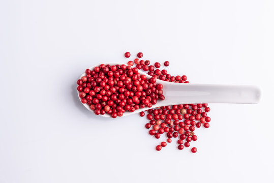 White spoon with Pink Pepper, Brazil Pepper, Rose pepper, Schinus terebinthifolius seeds over white background, top view