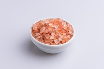 Fototapeta na wymiar Pink himalayan salt on white bowl and on white background - isolated, angle view, copy space, soft light