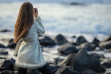 A young girl on the shore of a stormy sea is photographed on a tourist trip around Sakhalin Island walking along the shore admiring nature.