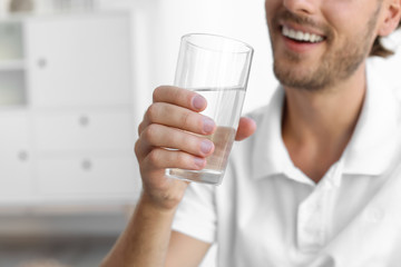 Young man holding glass of clean water indoors, closeup. Space for text