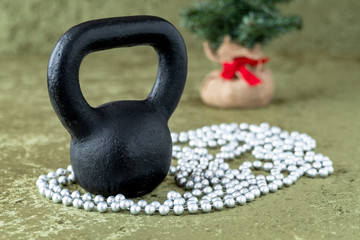 Obraz na płótnie Canvas Black kettlebell on a green velvet background with silver bead garland, holiday fitness, Christmas tree in background