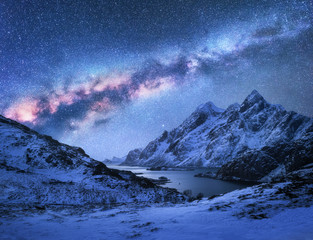 Bright Milky Way over snow covered mountains and sea bay at night in winter in Norway. Spectacular landscape with snowy rocks, starry sky, colorful milky way, beautiful fjord. Lofoten Islands. Space