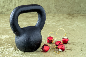 Obraz na płótnie Canvas Black kettlebell on a green velvet background with red jingle bells on gold thread, holiday fitness
