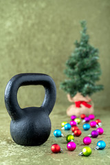 Naklejka na ściany i meble Black kettlebell on a green velvet background with colorful ball ornaments, holiday fitness, Christmas tree in background