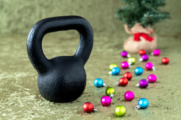Fototapeta na wymiar Black kettlebell on a green velvet background with colorful ball ornaments, holiday fitness, Christmas tree in background