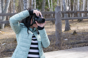 Girl photographer in autumn jacket taking pictures of objects standing on in the woods on the road...