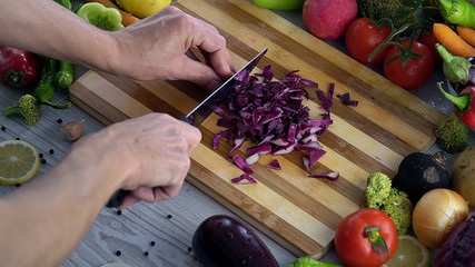 Man is cutting vegetables in the kitchen, slicing red cabbage