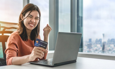 Young asian woman holding credit card and use laptop for purchase product on internet in home...
