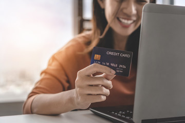 Young asian woman holding credit card and use laptop for purchase product on internet in home office, Cyber Monday shopping online concept.