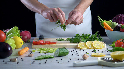 Man is cutting  parsley on the cutting board