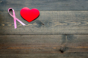 Breast cancer. Mammalogy concept. Symbolic pink ribbon near heart sign on dark wooden background top view space for text