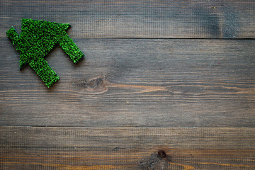 Eco friendly technologies for home concept. House silhouette made of green grass on dark wooden background top view copy space
