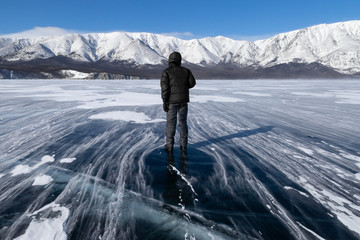 A man standing on beautiful smooth surface of frozen mountain lake during a strong wind in winter. Scenic landscape or background