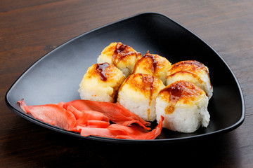 Baked sushi in a black plate. A plate on a dark wooden background, in a plate of sushi and ginger.