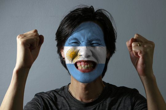 Cheerful portrait of a man with the flag of the Argentina painted on his face on grey background. The concept of sport or nationalism.