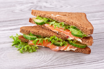 Sandwich with bread toasts, red fish salmon, fresh green leaves of salad and sliced cucumber