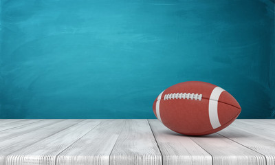 3d rendering of a ball for American football lying on a wooden desk on a blue background.
