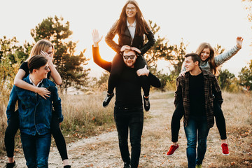 Three young men giving piggyback ride to lovely girlfriends while walking along countryside path...
