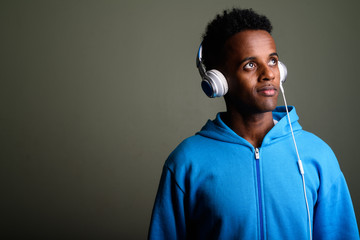 Fototapeta premium Young handsome African man listening to music against colored ba