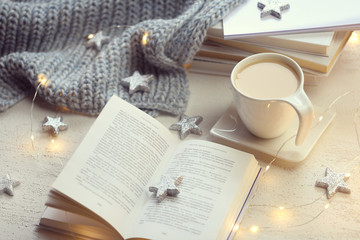 Winter books. Winter cozy reading. open book,  gray knitted scarf,  cup of coffee, shining garland...