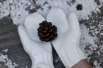 hands in white mittens hold a large lump on the background of a snow-covered wooden surface