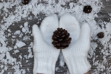 hands in white mittens hold a large lump on the background of a snow-covered wooden surface