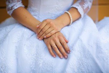 The palm of the bride with a ring and a bracelet on the background of a white dress