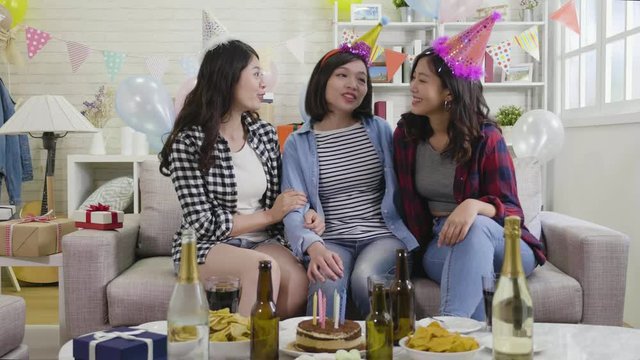 slow motion of young asian girlfriends sitting on couch cheerfully talking and hugging with love. group of best friends at house party celebrating birthday in the day. happy ladies enjoy gathering.