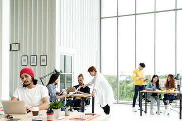 Successful multiethnic business team in routine work creative lifestyle standing, sitting and talking together at modern office with wide angle view. Young busy diverse teamwork or employees concept.