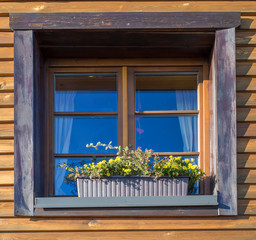 Fototapeta na wymiar Window of old brown wooden mountain cottage house with blooming flower pot
